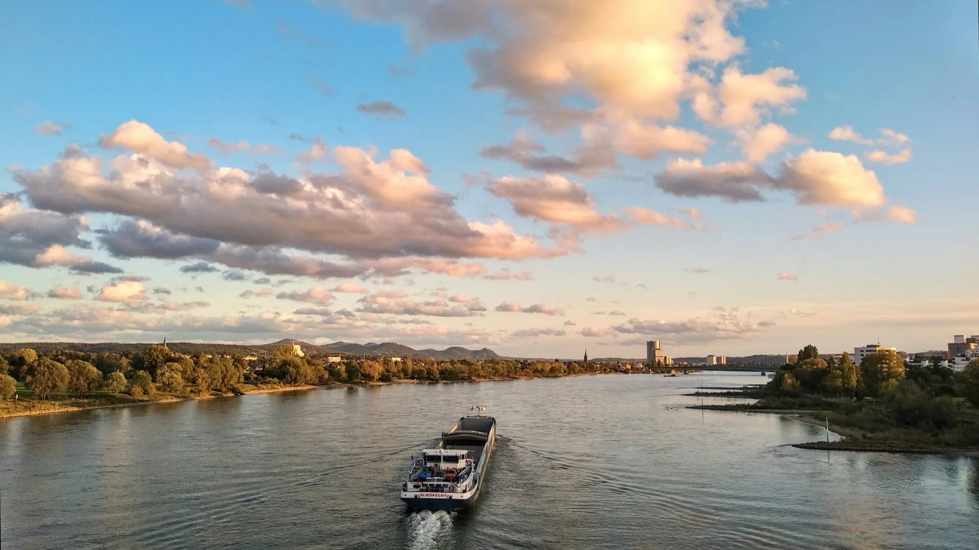 Binnenvaartschip op een brede rivier bij zonsondergang